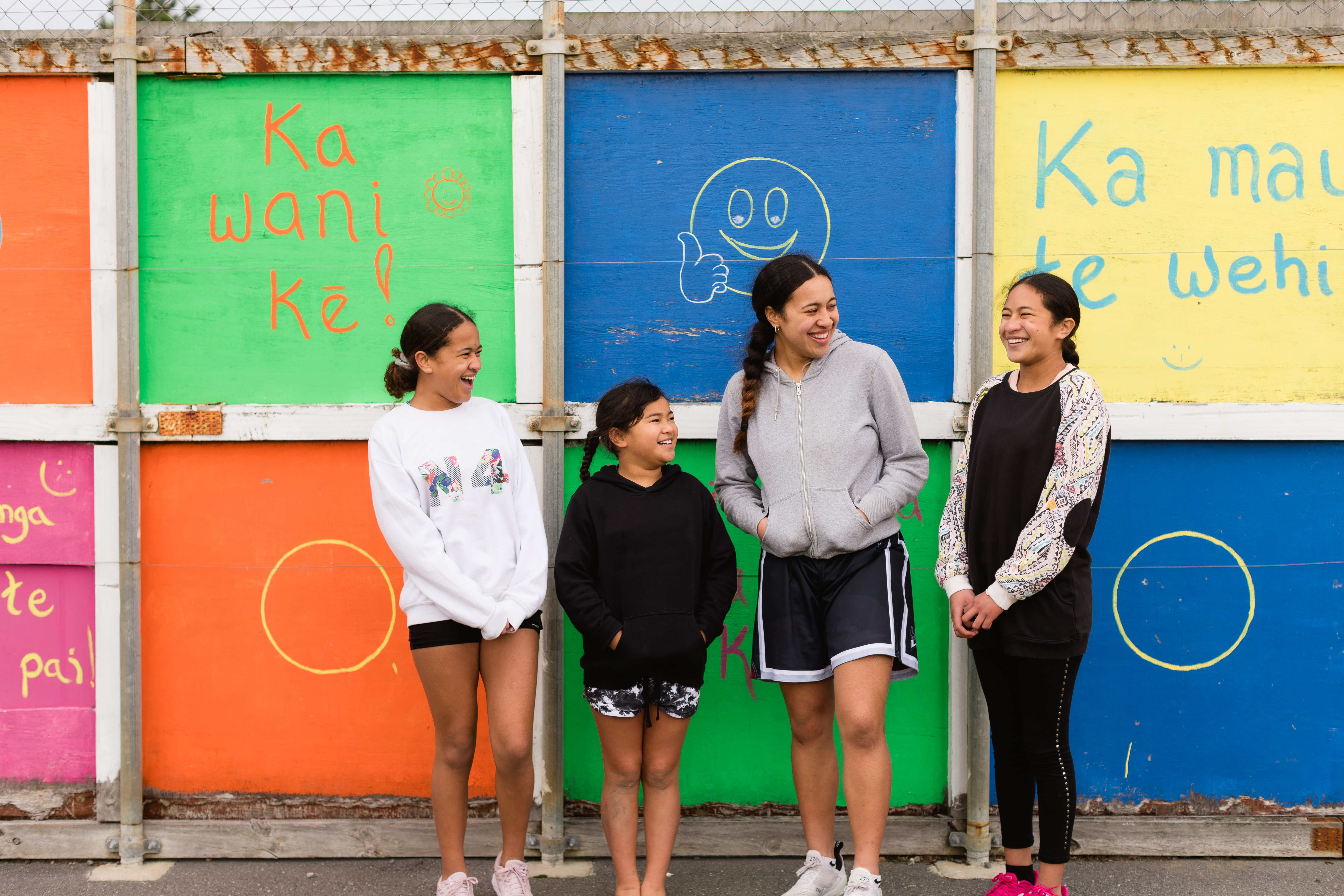 4 girls laughing in front of a colourful wall